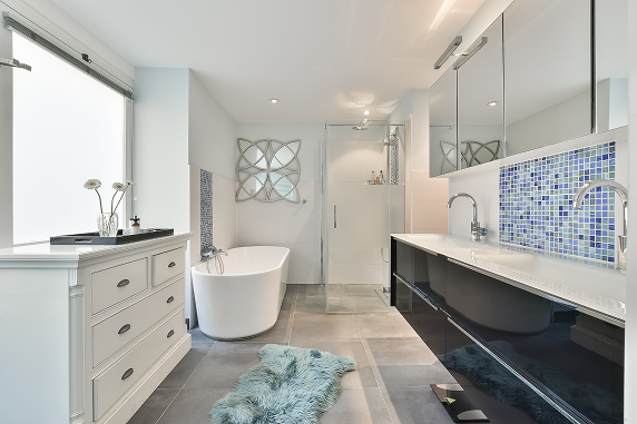 Modern bathroom with a freestanding tub, glass shower, and double sink. Blue mosaic backsplash and a fluffy rug add a serene, stylish touch.