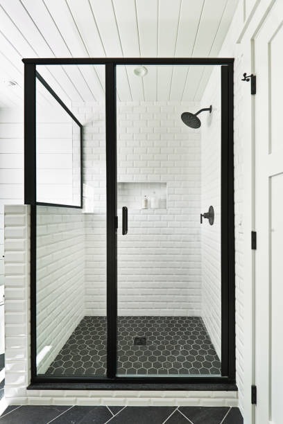 Modern shower with square black rainfall showerhead, glass door, and marble-patterned tiles. The space feels sleek and luxurious.
