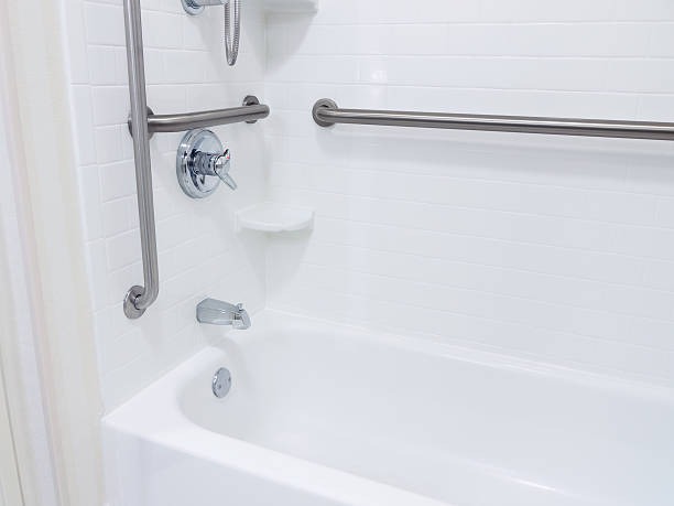 White bathroom with a bathtub featuring silver grab bars, a showerhead, and faucet. White tiles create a clean, accessible, and modern look.